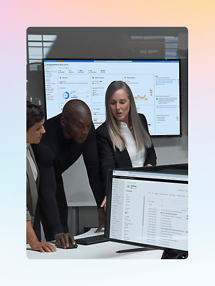 Three people are standing around a desk, looking at a computer screen with data displayed on it