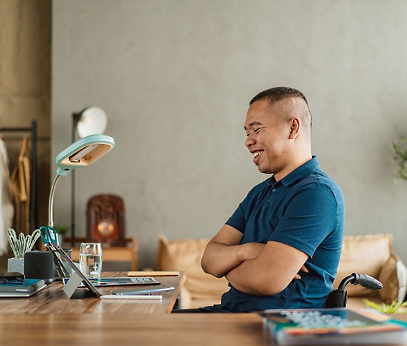 Мужчина улыбается цифровому планшету на столе в тепло освещенном домашнем офисе.