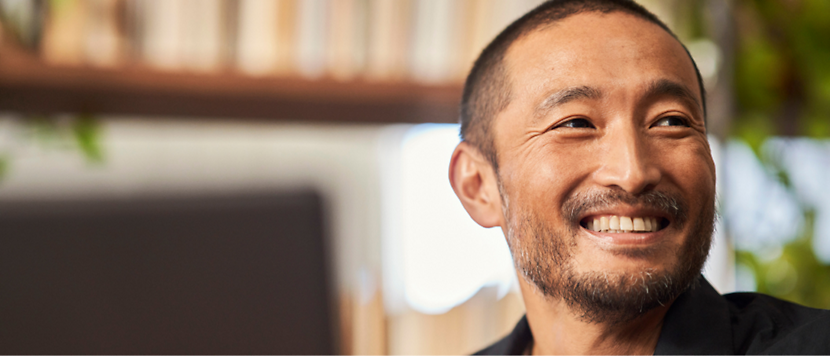 Smiling man in a black shirt with a blurred bookshelf in the background.