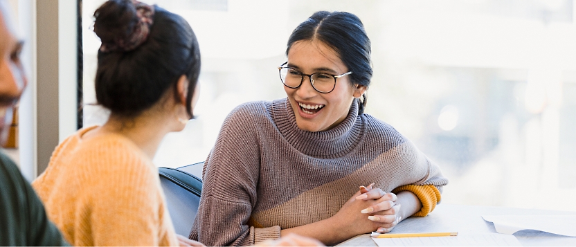 Two people seated at a table, engaged in a lively conversation. One person is wearing glasses and a sweater