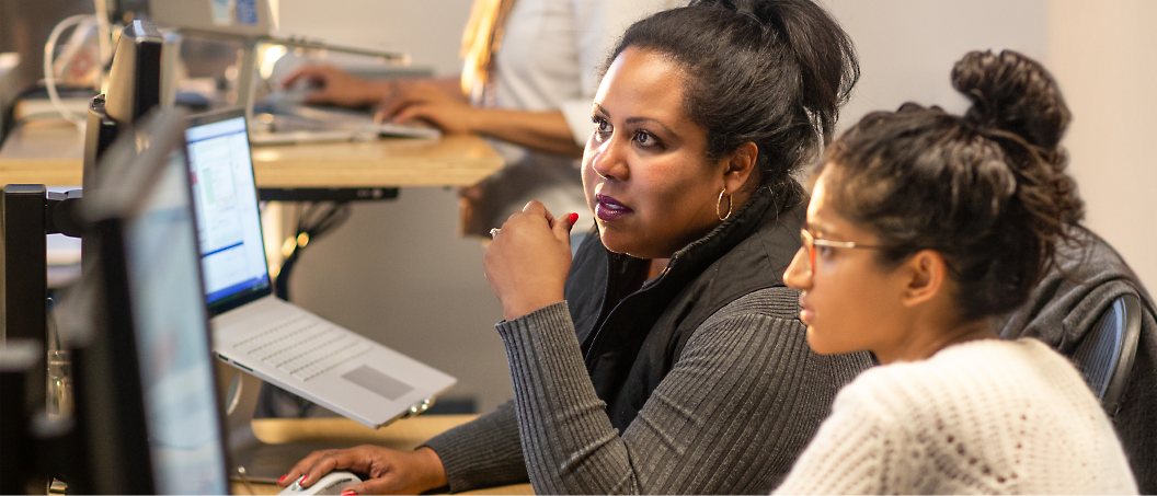 Two women working at a computer. The woman on the left is pointing at the screen, while the woman on the right 