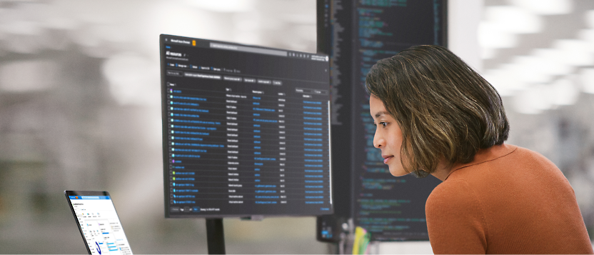 A person working on multiple computer screens displaying code and data in an office environment.