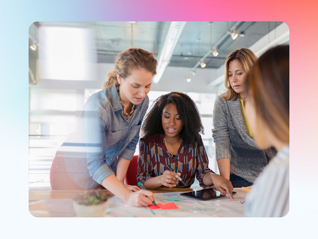 Four women collaborating over documents on a table in a brightly lit office.