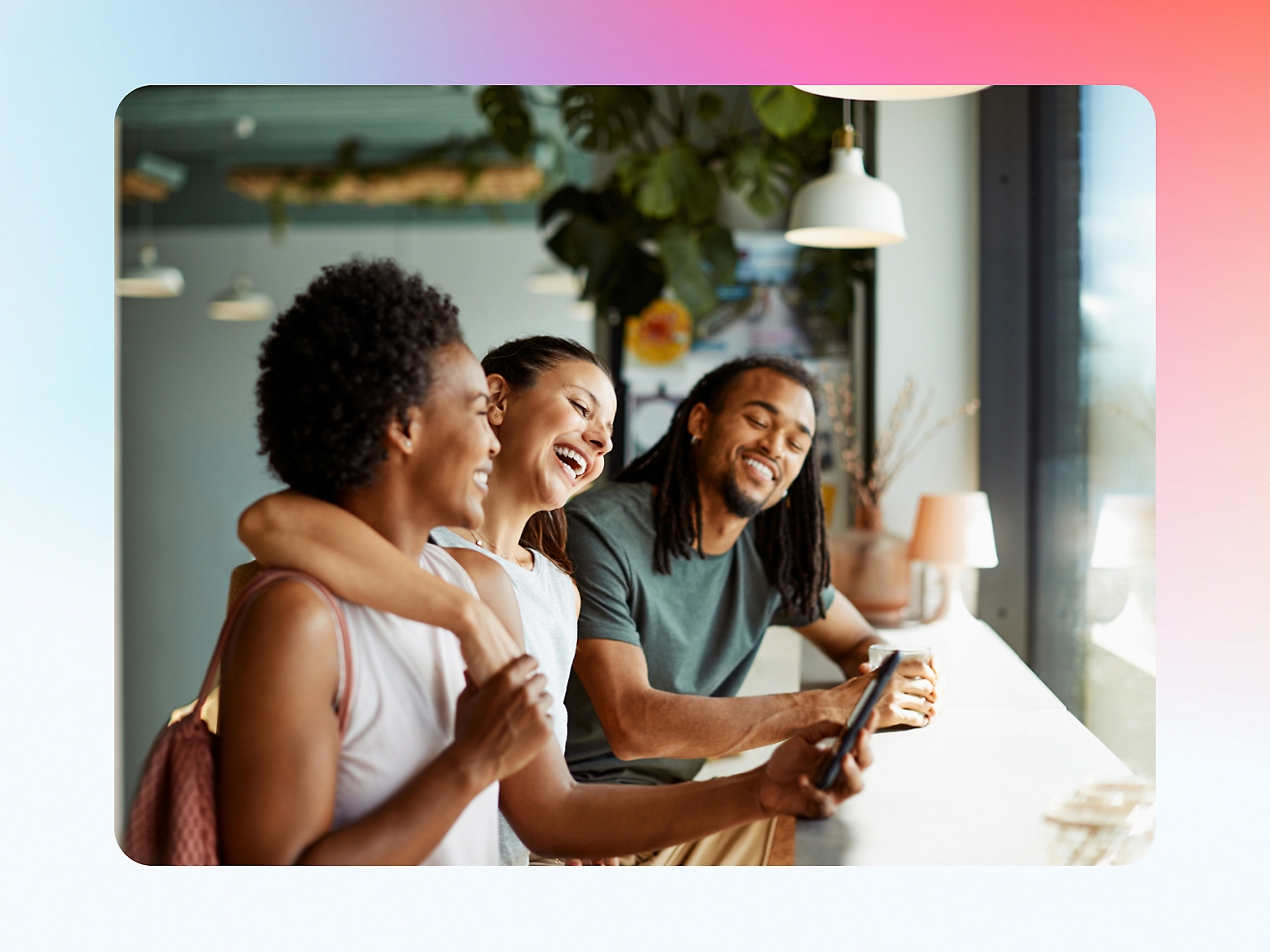 Three friends laughing and looking at a smartphone together in a modern café.