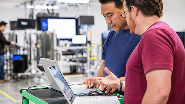 Two professionals discussing work on a laptop in an industrial setting.