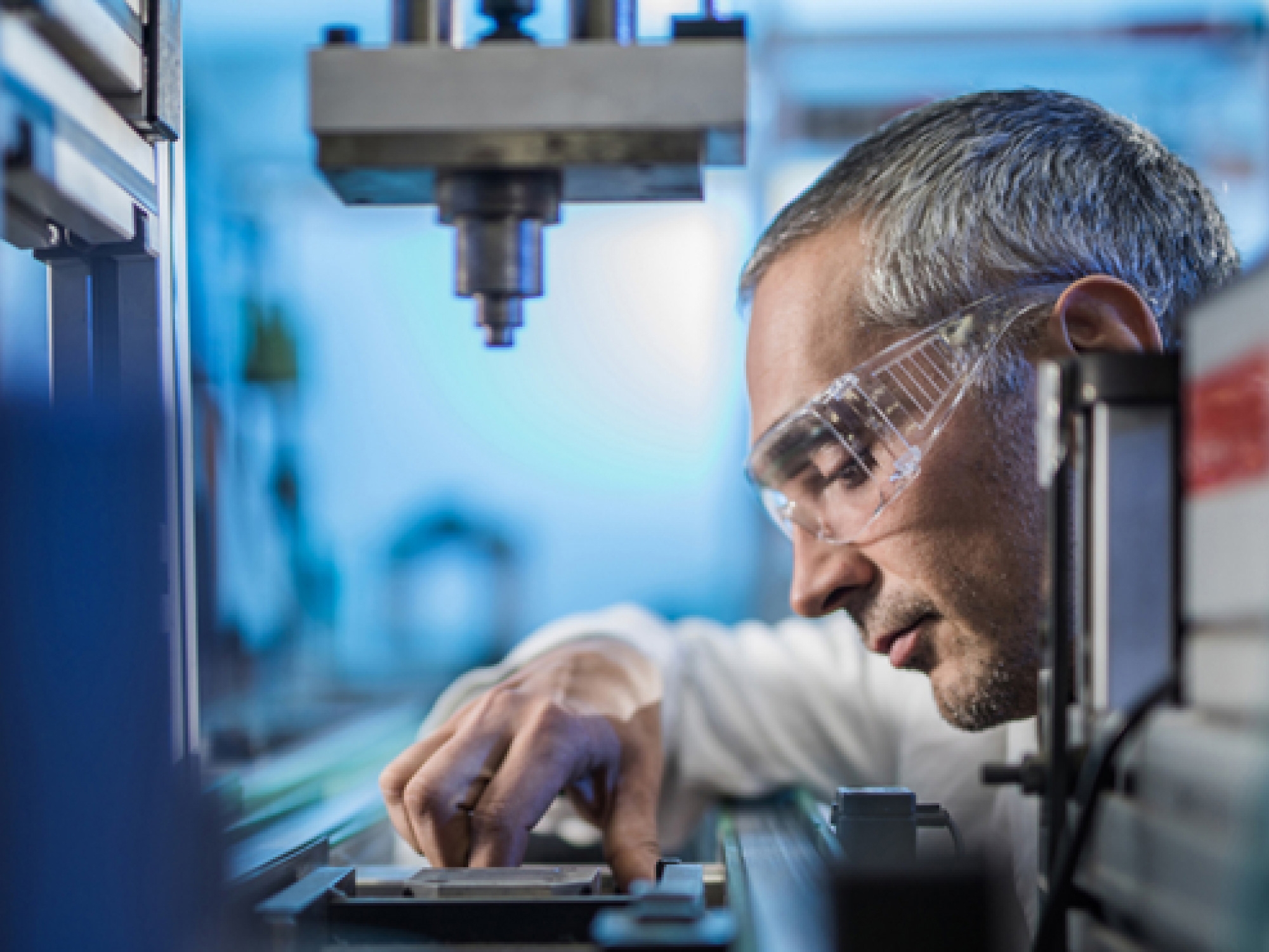 A technician wearing safety glasses carefully adjusts equipment in a laboratory setting.