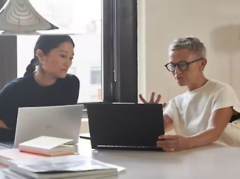 Two people sitting, looking at a laptop and having a discussion on some topic.