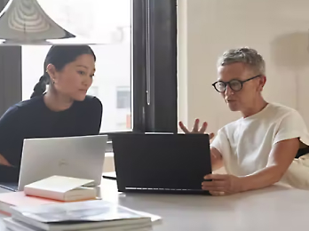 To personer sitter og ser på en bærbar datamaskin, og diskuterer om et emne.
