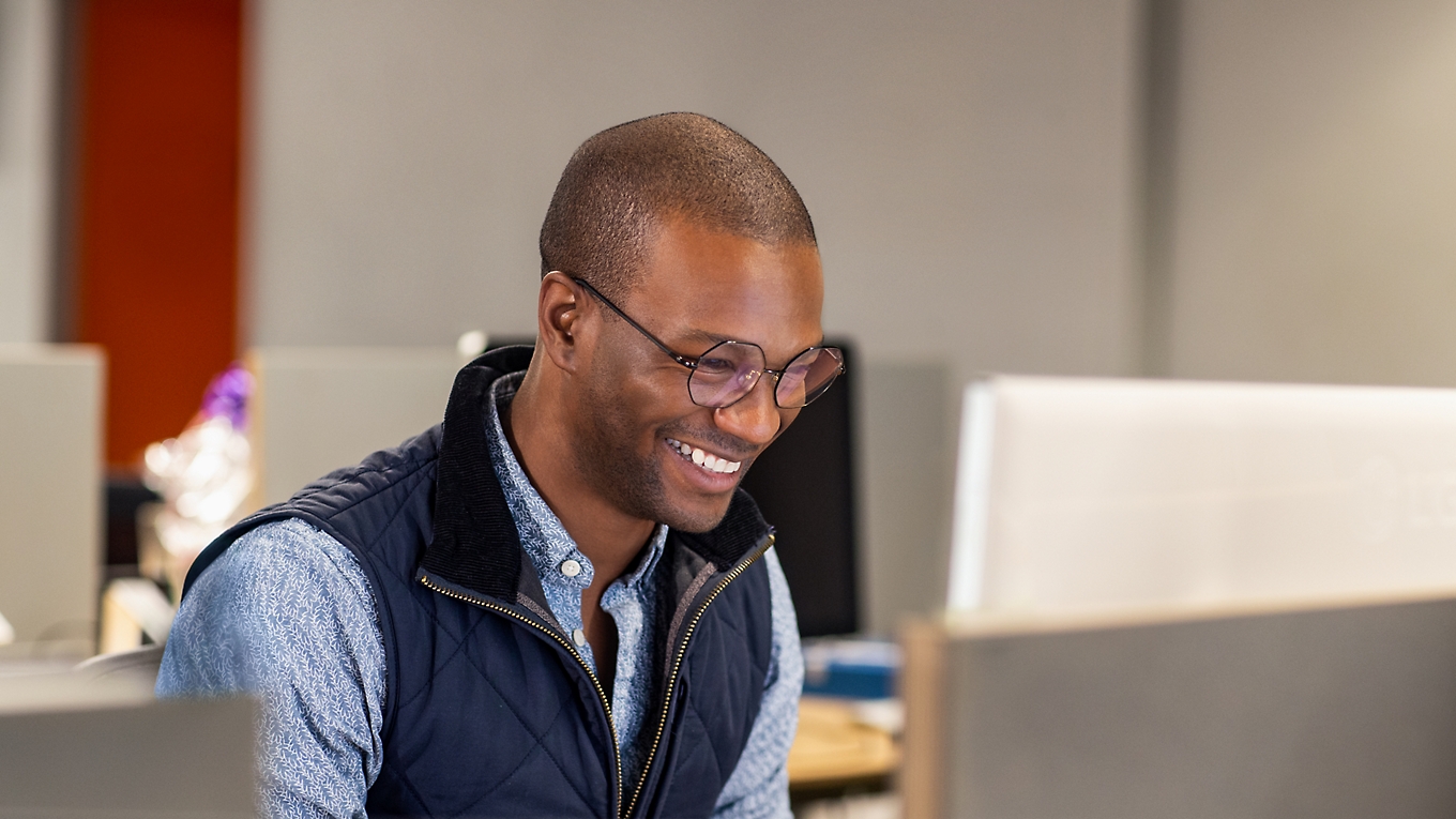 A person sitting in the office smiling and working with a laptop