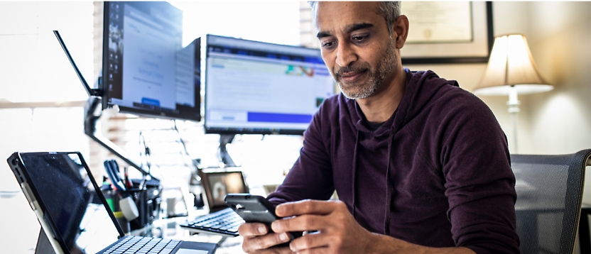 Een man die aan een bureau zit en een mobiele telefoon gebruikt.