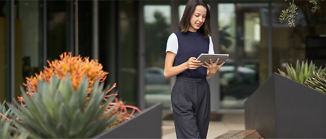 A woman reading from a tablet while standing outside a building.