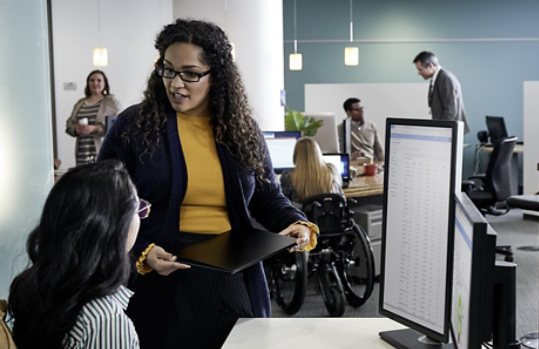 A person uses a Surface device with a co-worker at the office.