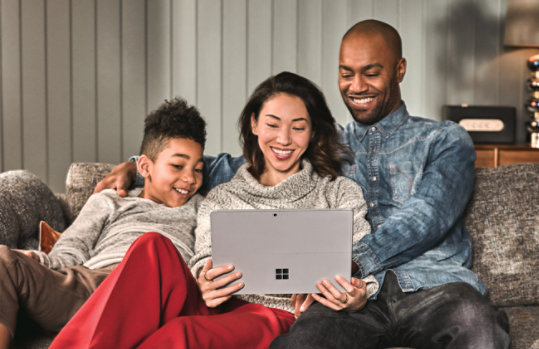  Rodzina siedząca na kanapie, używająca razem laptopa Surface.