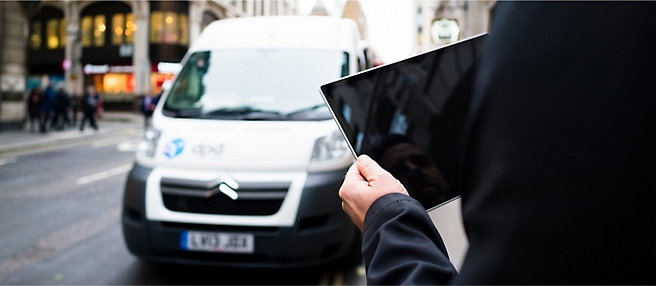 Een man die voor een busje staat en een tablet vasthoudt.