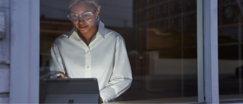 A woman in glasses is using a tablet computer in front of a window.