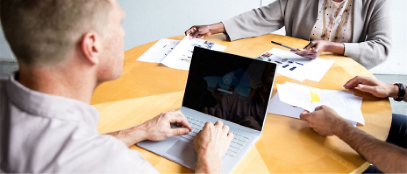 A group of people sitting around a table with a laptop.