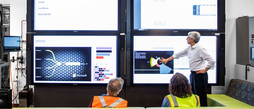 A group of people standing in front of a large screen.