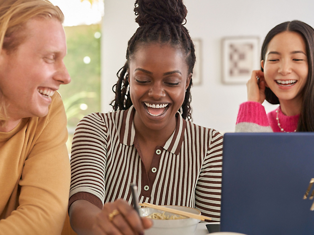 A group of people laughing and looking at a computer