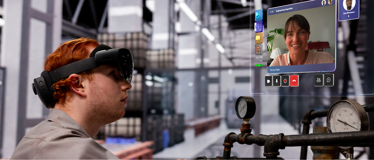 A person wearing AR glasses in an industrial setting interacts with a virtual screen showing a video call with a smiling person. 