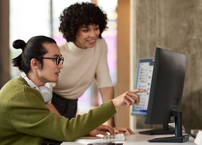 Two people are working at a desk, looking at a computer screen.