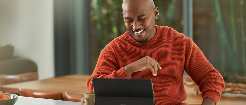 A person is sitting at a table, smiling while looking at a tablet