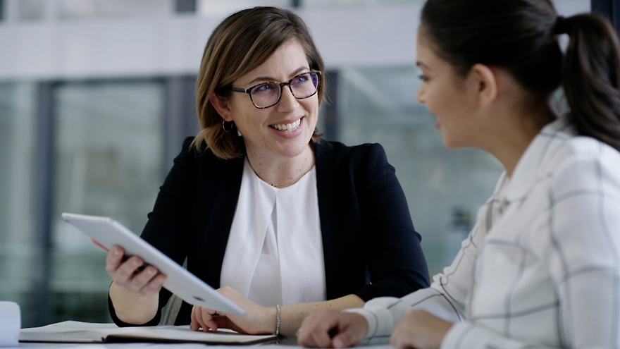 Two business women talking at a table with a tablet.