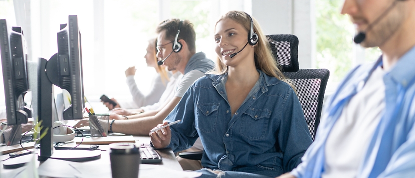 Een persoon die een headset draagt en aan een bureau zit