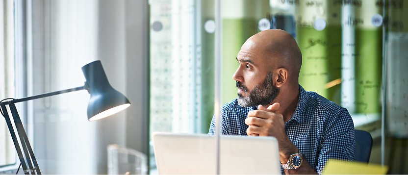 Een persoon die op kantoor zit en naar buiten kijkt met zijn laptop open op tafel