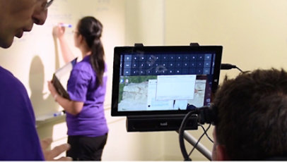 Someone appears to use eye tracker while a woman writes on a whiteboard.