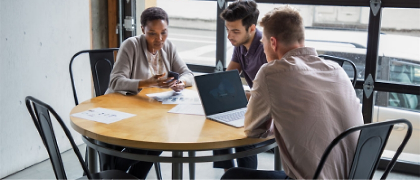 A group of people sitting around a table with laptops.