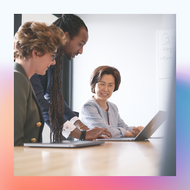 Three professionals engaged in a collaborative discussion around a laptop in a modern office setting.