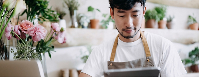 A person is using a tablet and flower vases are kept around.