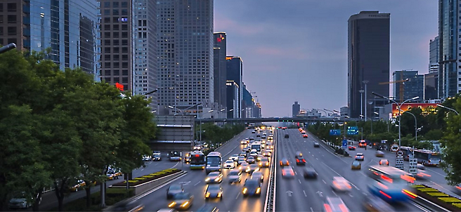 黃昏時多雲天空下的現代化摩天大樓列於多線道市區道路的兩側，而道路上的車子來往穿梭。