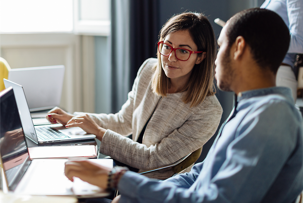 A man and woman sitting at desk looking at laptop screens