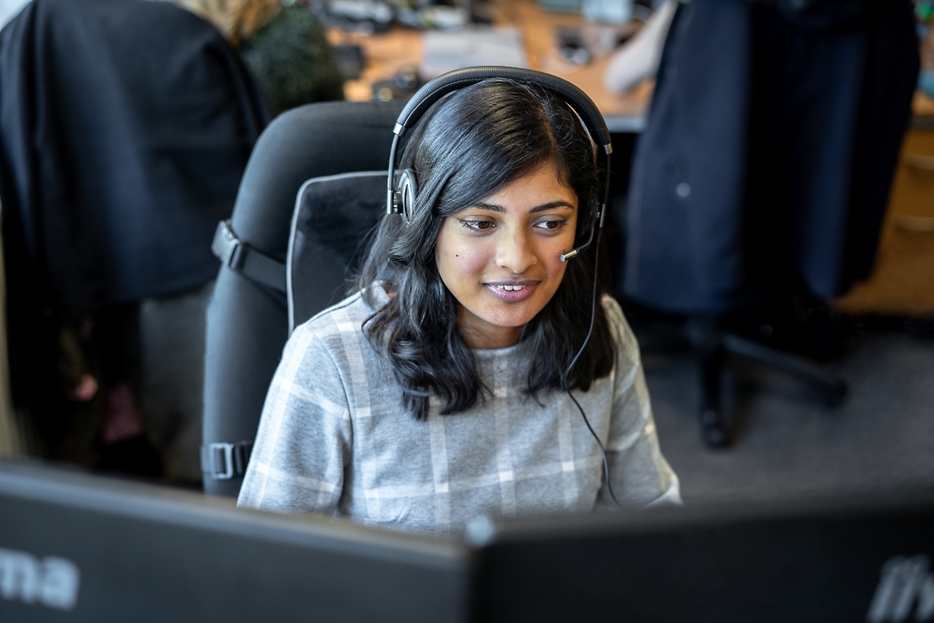 Een vrouw met een headset op die op een computer werkt.