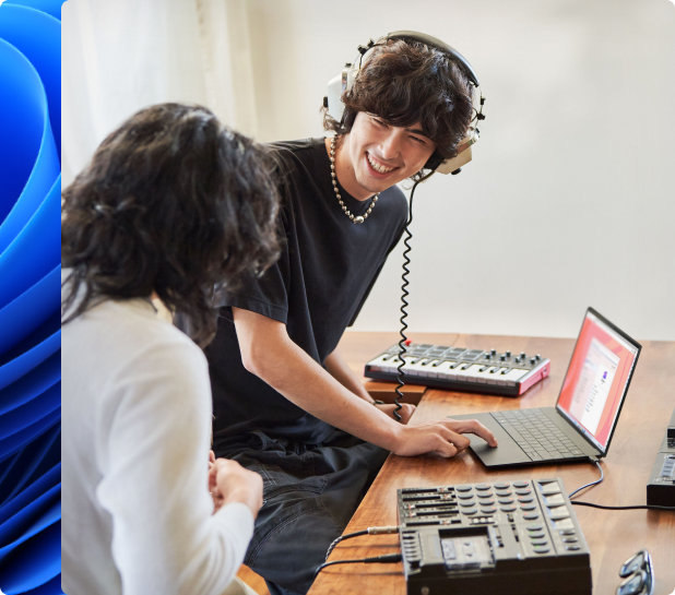 Ung mann smiler og har på hodetelefoner og en annen person lager musikk på en bærbar PC med et elektronisk keyboard