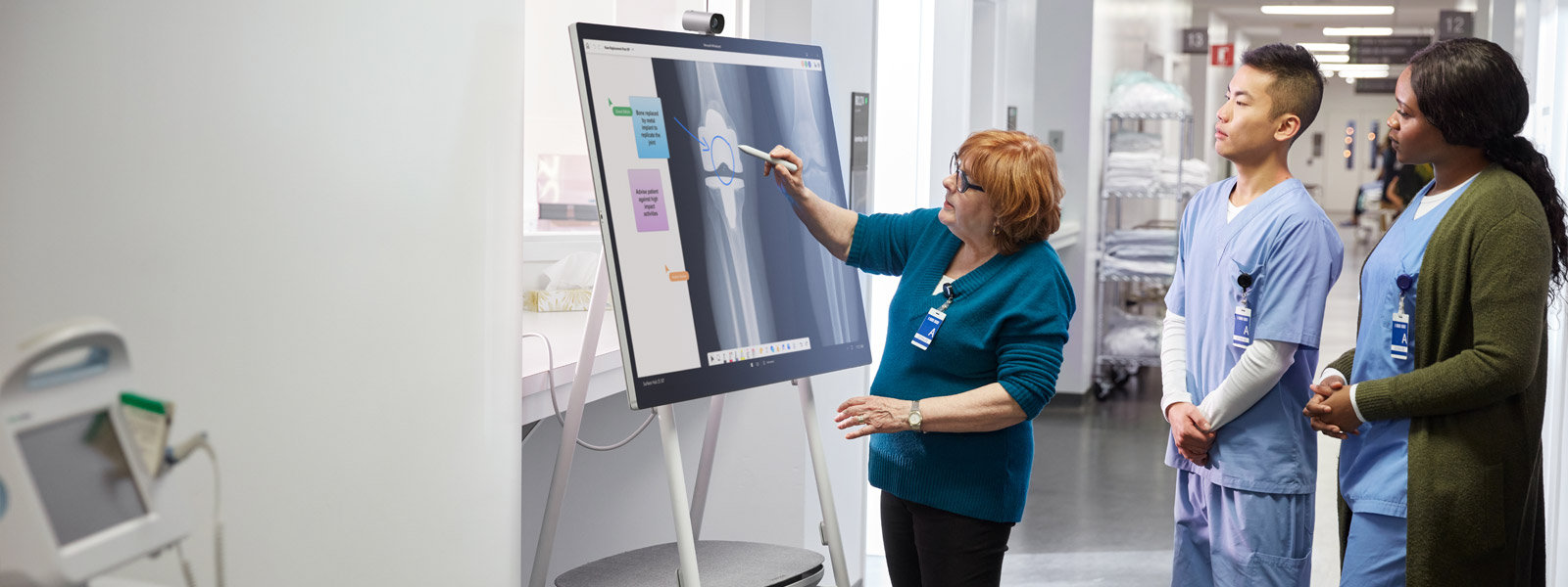 Una mujer interactúa con la pantalla de un dispositivo Surface Hub 2S mientras dos personas observan