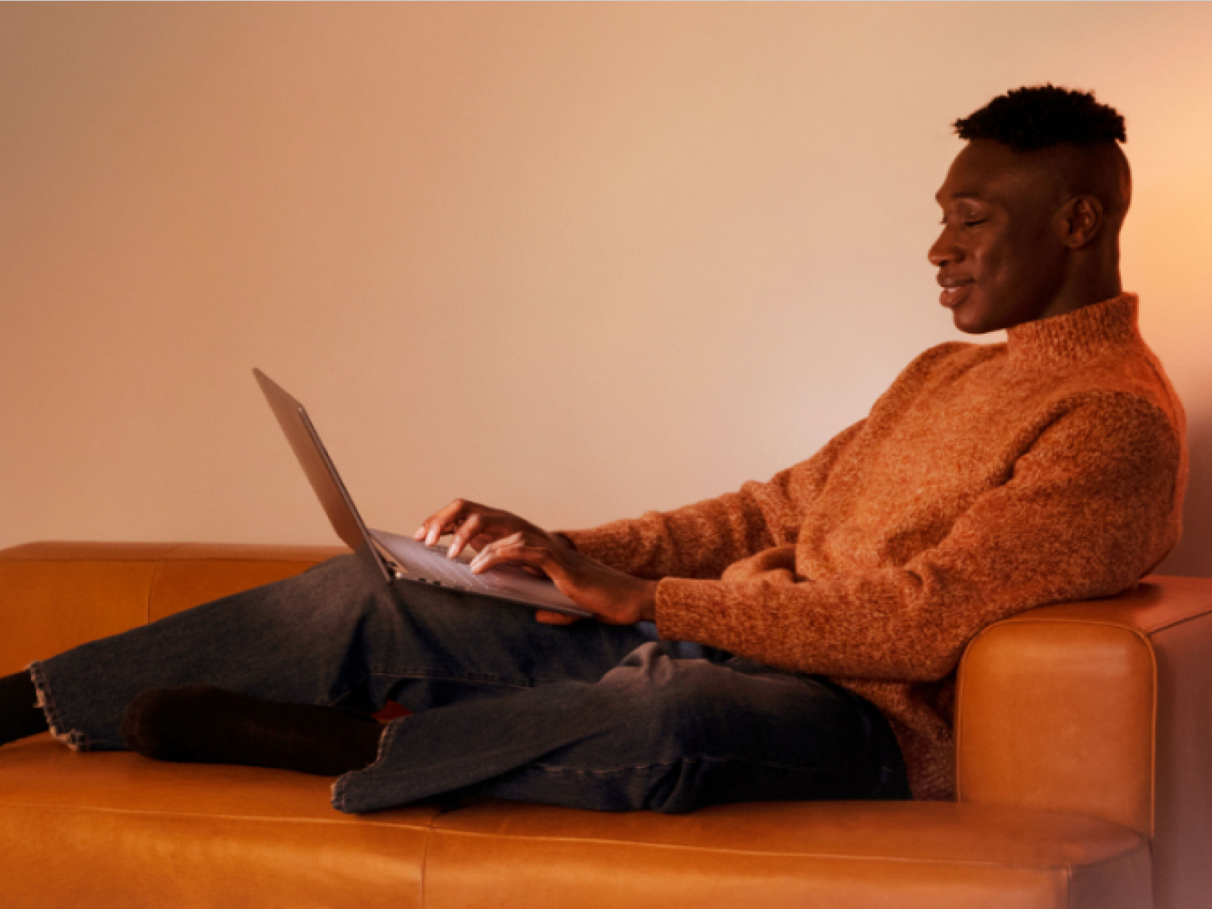 Un homme assis sur un divan orange utilisant son ordinateur portable