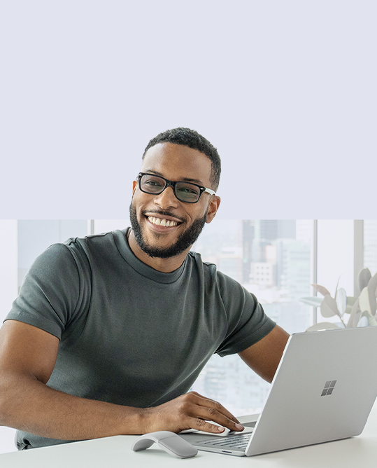 A man sits at his Surface Laptop 5 while looking off into the distance