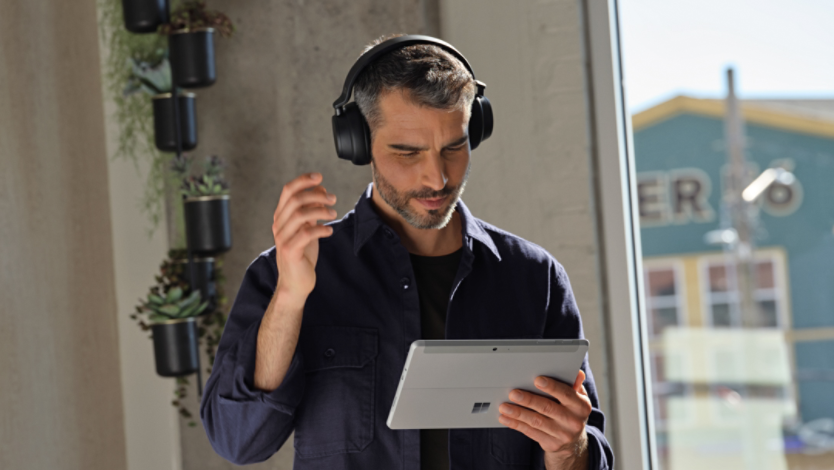 A man standing and listening to headphones while holding his Surface device