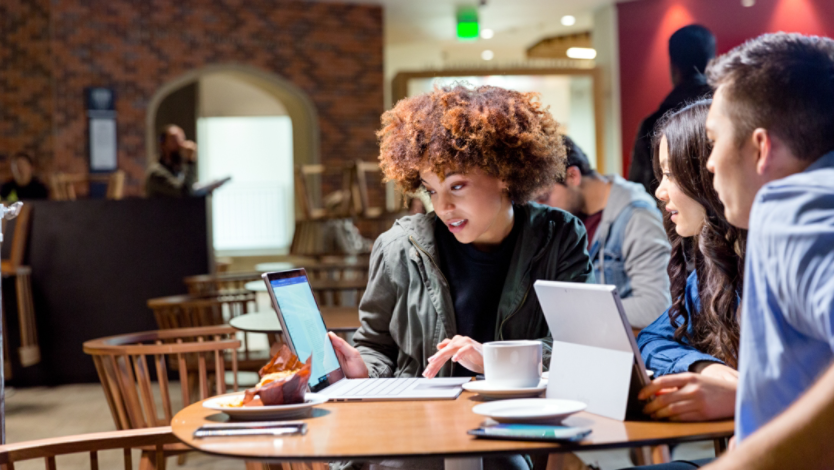 A group of students working together on a laptop and 2-in-1 PC in a dining hall