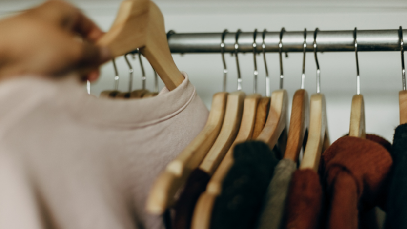 A person hand picking a shirt from clothing rack