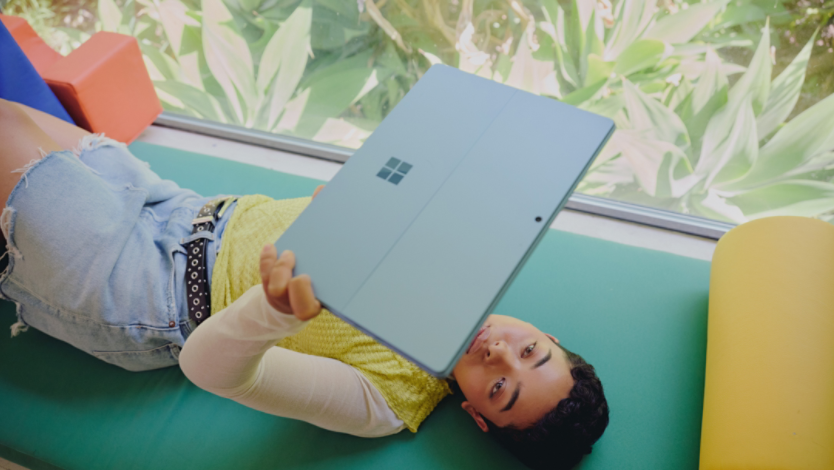 A woman laying down holding a surface device above her