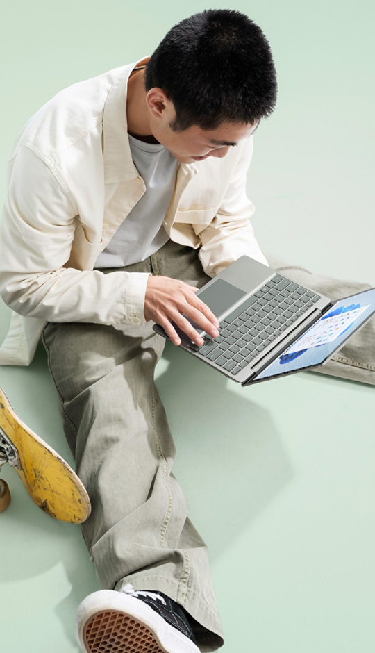 A young man takes a break from skateboarding to type a quick message on Surface Laptop Go 3.