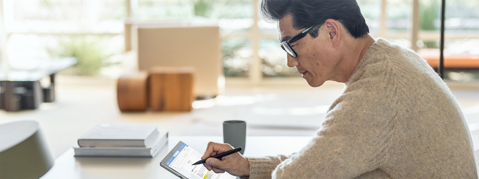 Un hombre sentado en una mesa usa un Lápiz para Surface con su dispositivo Surface