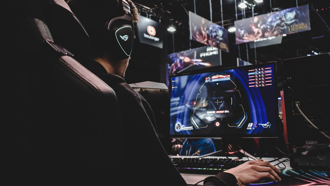 Man wearing headphones sits in an event venue in front of a PC desktop streaming a video game