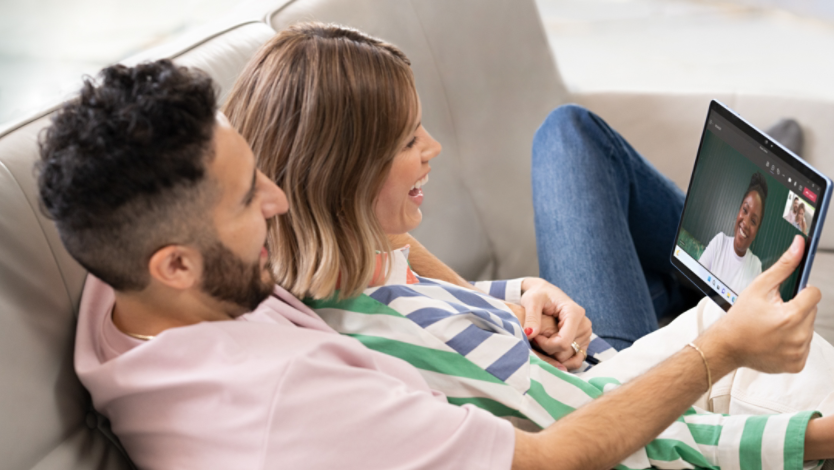 Two people lying together on a couch, video calling on their Surface device