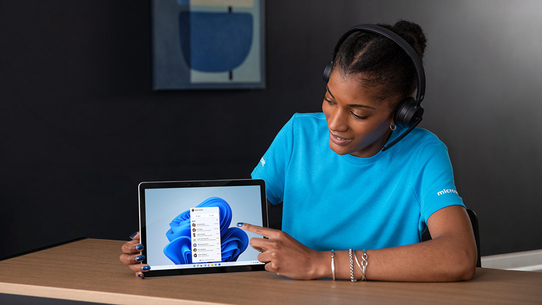 Woman wearing a blue shirt, wearing a headset, pointing to a PC