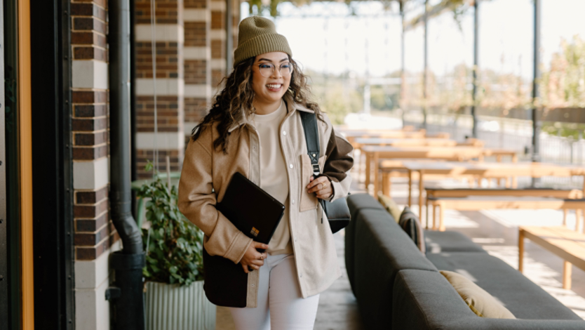 woman in outdoor restaurant holding Surface laptop and backpack