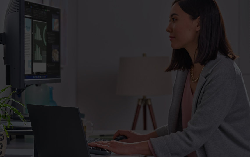 Woman looking at monitor on swivel mount with a laptop on desk to the side